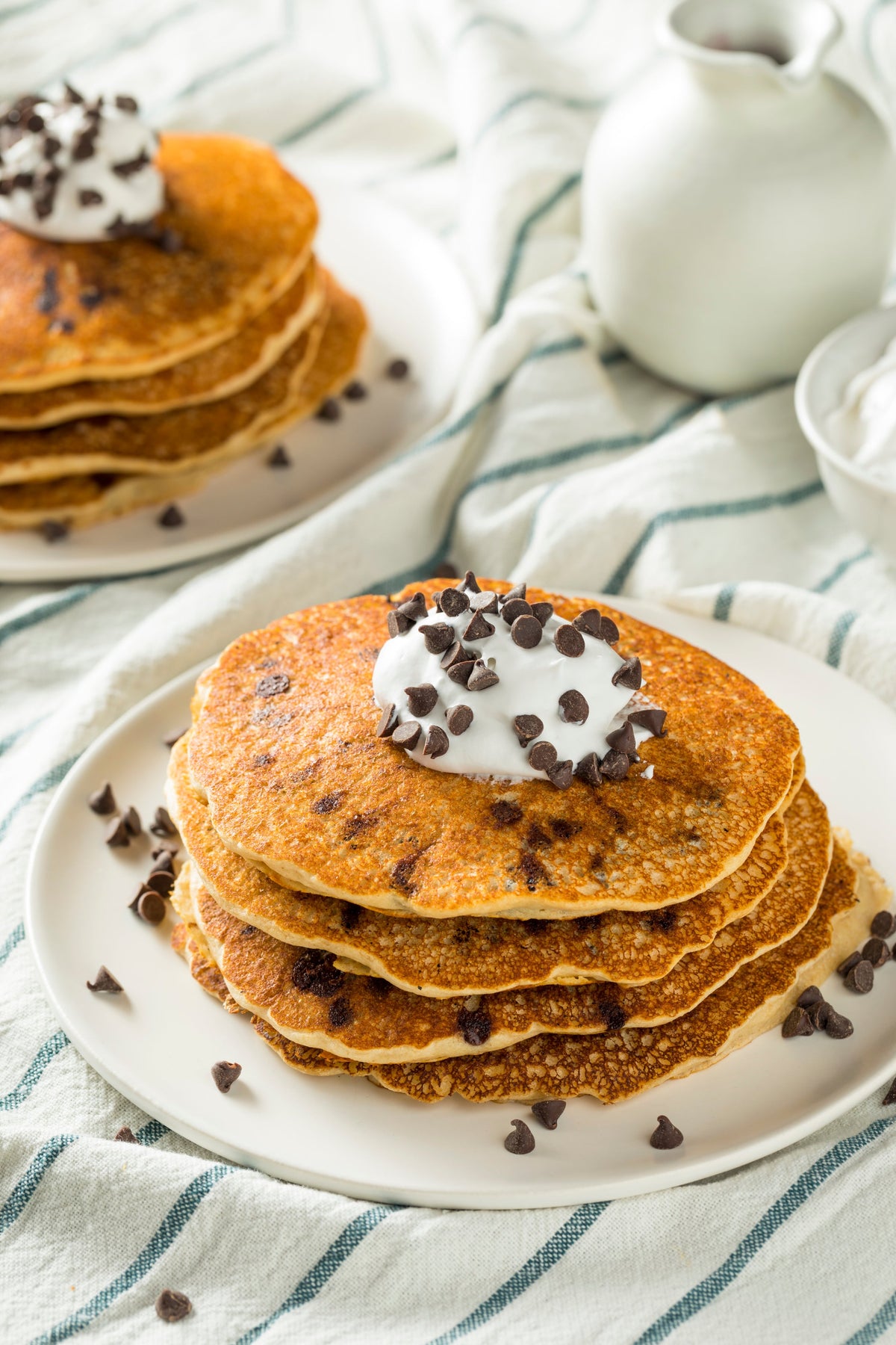 2 plates of chocolate chip pancake with whipped cream and chocolate chips on top.