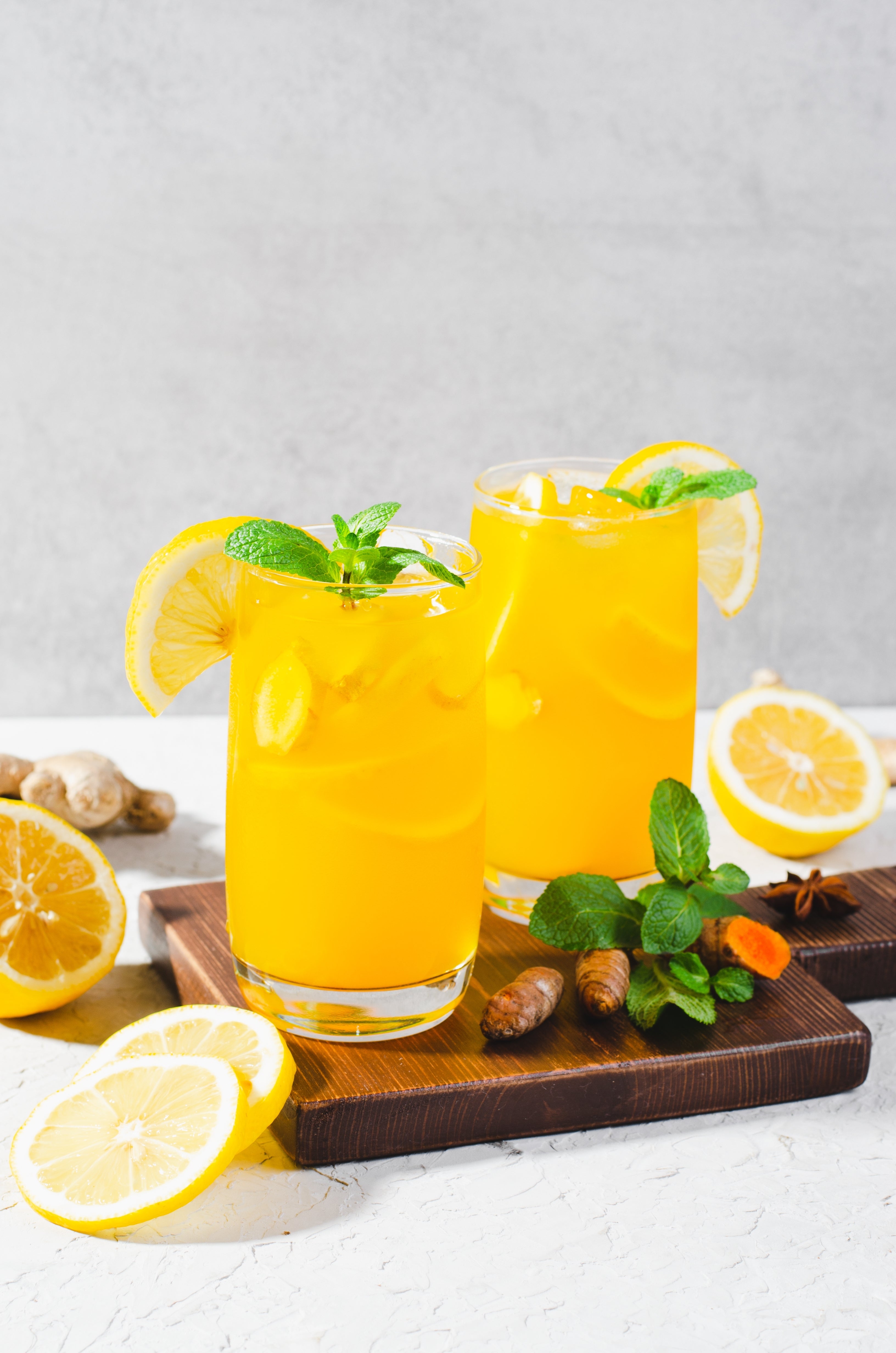 2 glasses of Lemon Ginger Turmeric Wellness Drink with lemon slices and ginger pieces at the side.