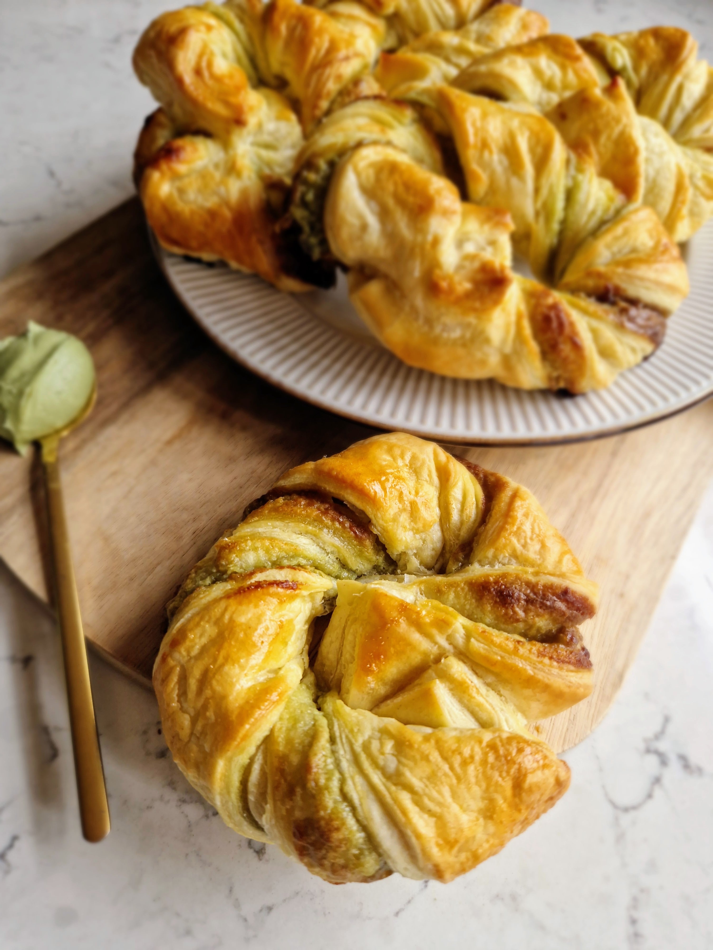 Pistachio Pastry swirls placed in a plate, along with a spoon of pistachio at the side