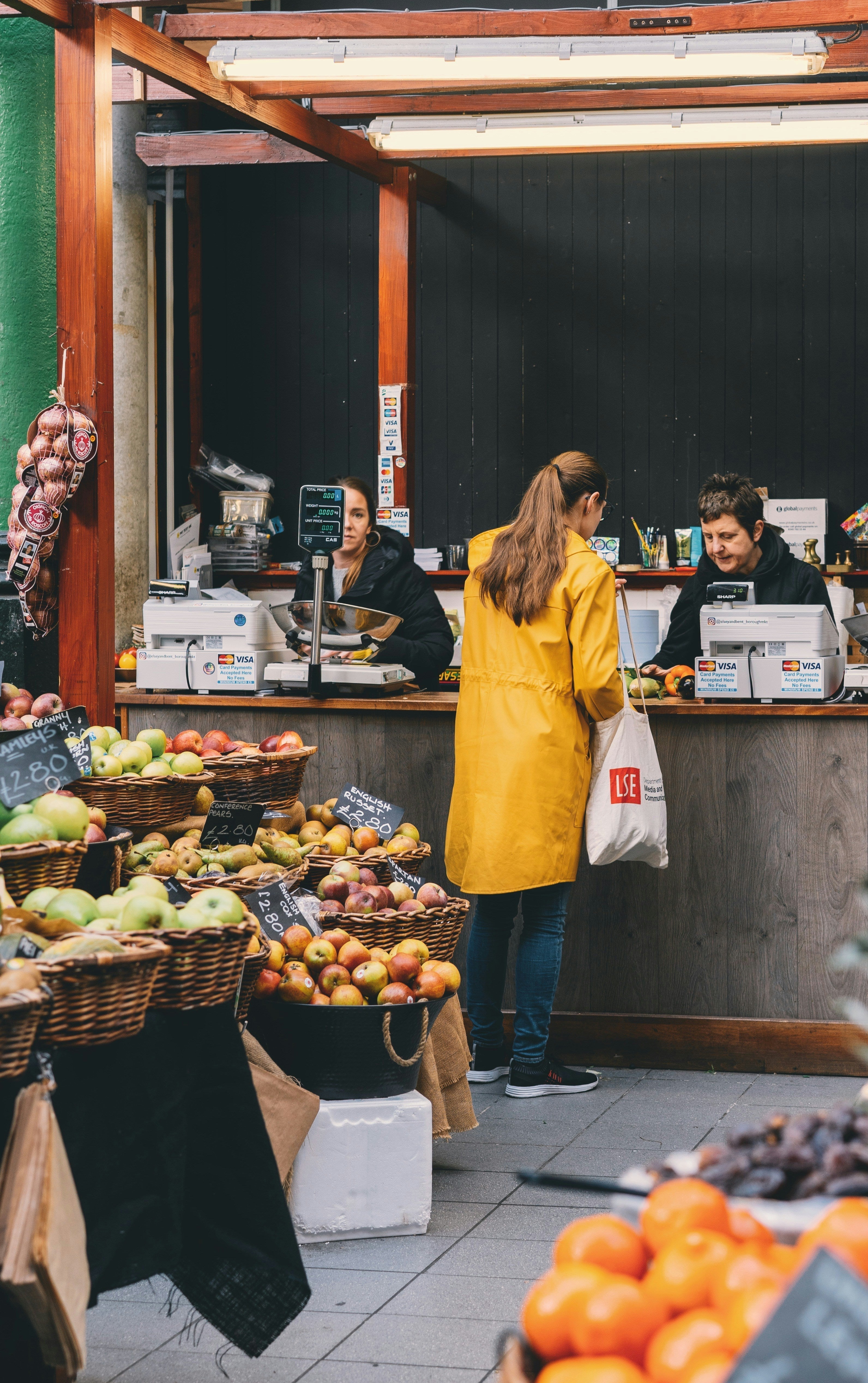 women paying at fruit market for shopping in bright yellow jacket