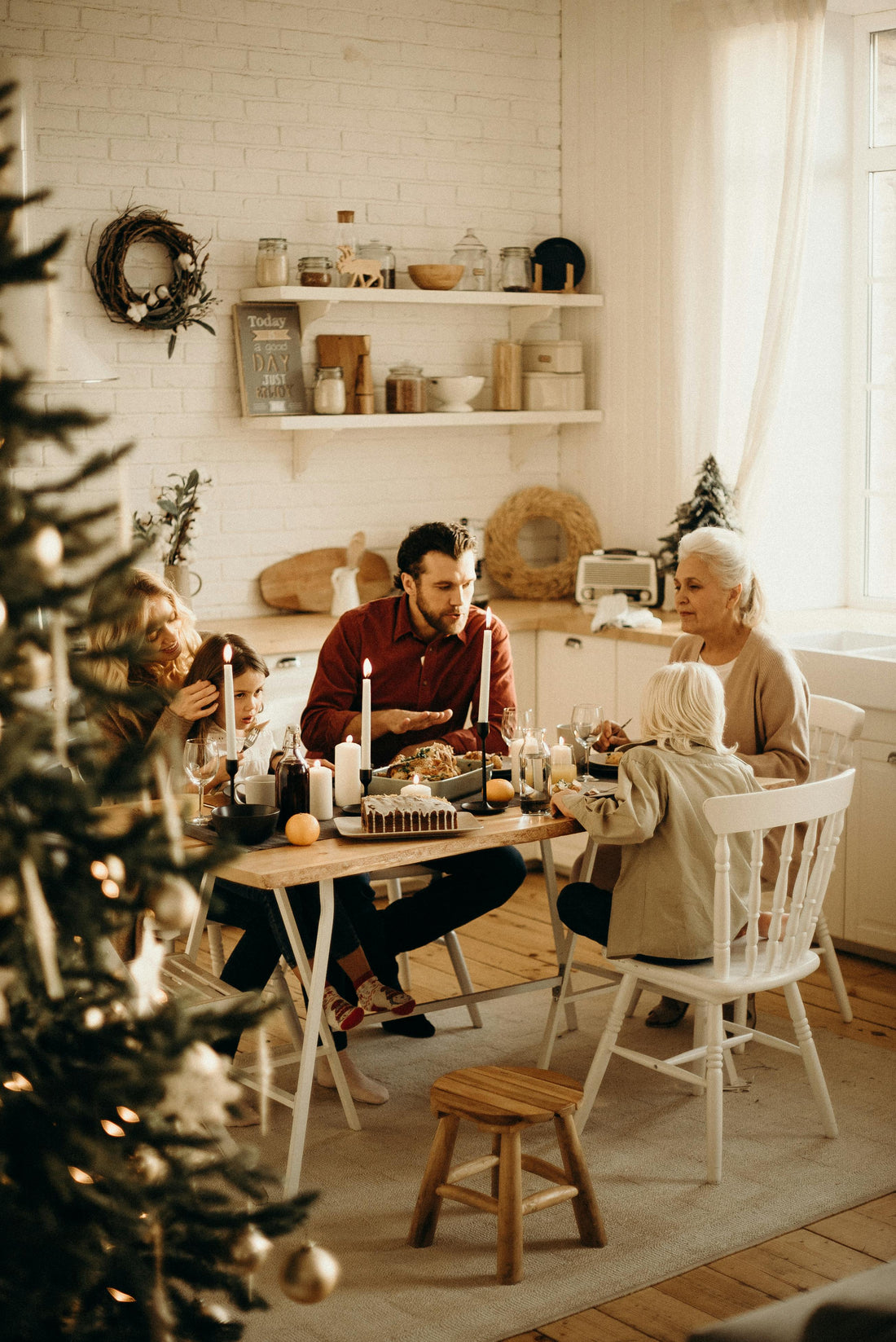 a family sitting around a table with a Christmas tree in the background