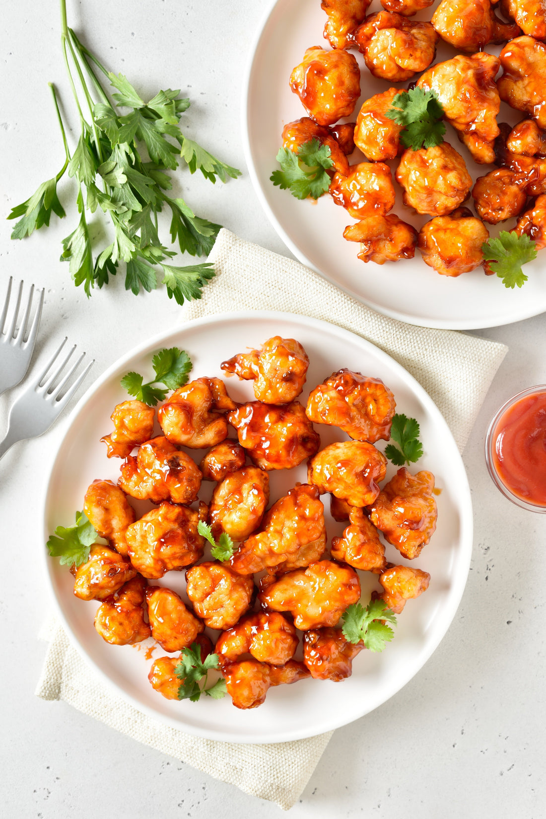 2 plates of Korean Fried Cauliflowers and some cilantro for decoration beside the plate in a white table.