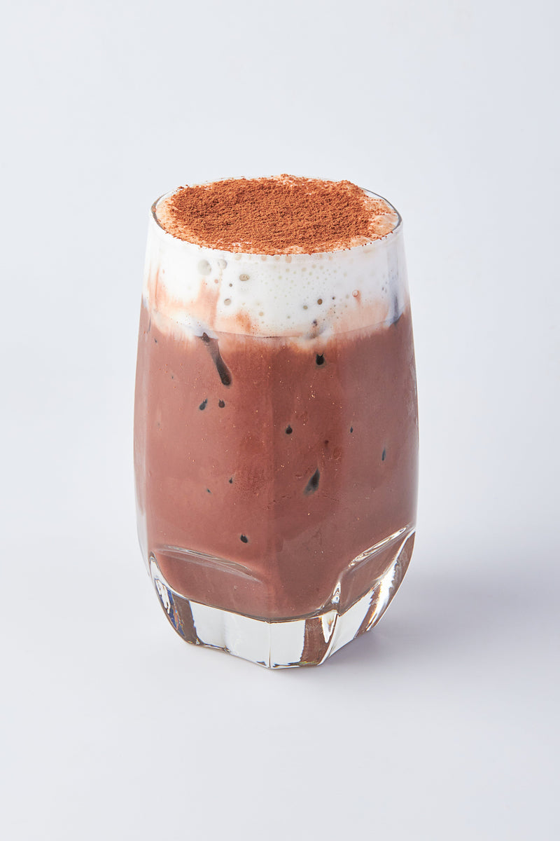 A cup Milo mocha layered with cream and chocolate dusting on top in a white background.