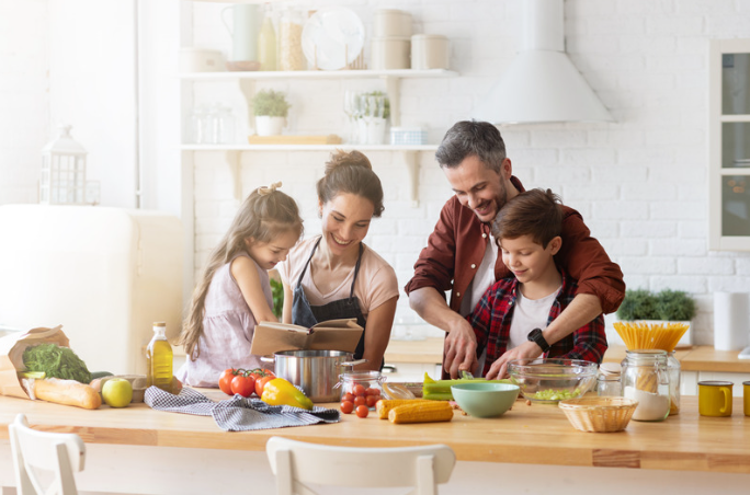 A happy family including mother, father, daughter and son cooking together in a kitchen.
