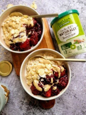 Two bowls of creamy berry tahini overnight oats topped with flaked almonds and served with Natvia 100% Natural Synbiotic Sweetener canister on the side.