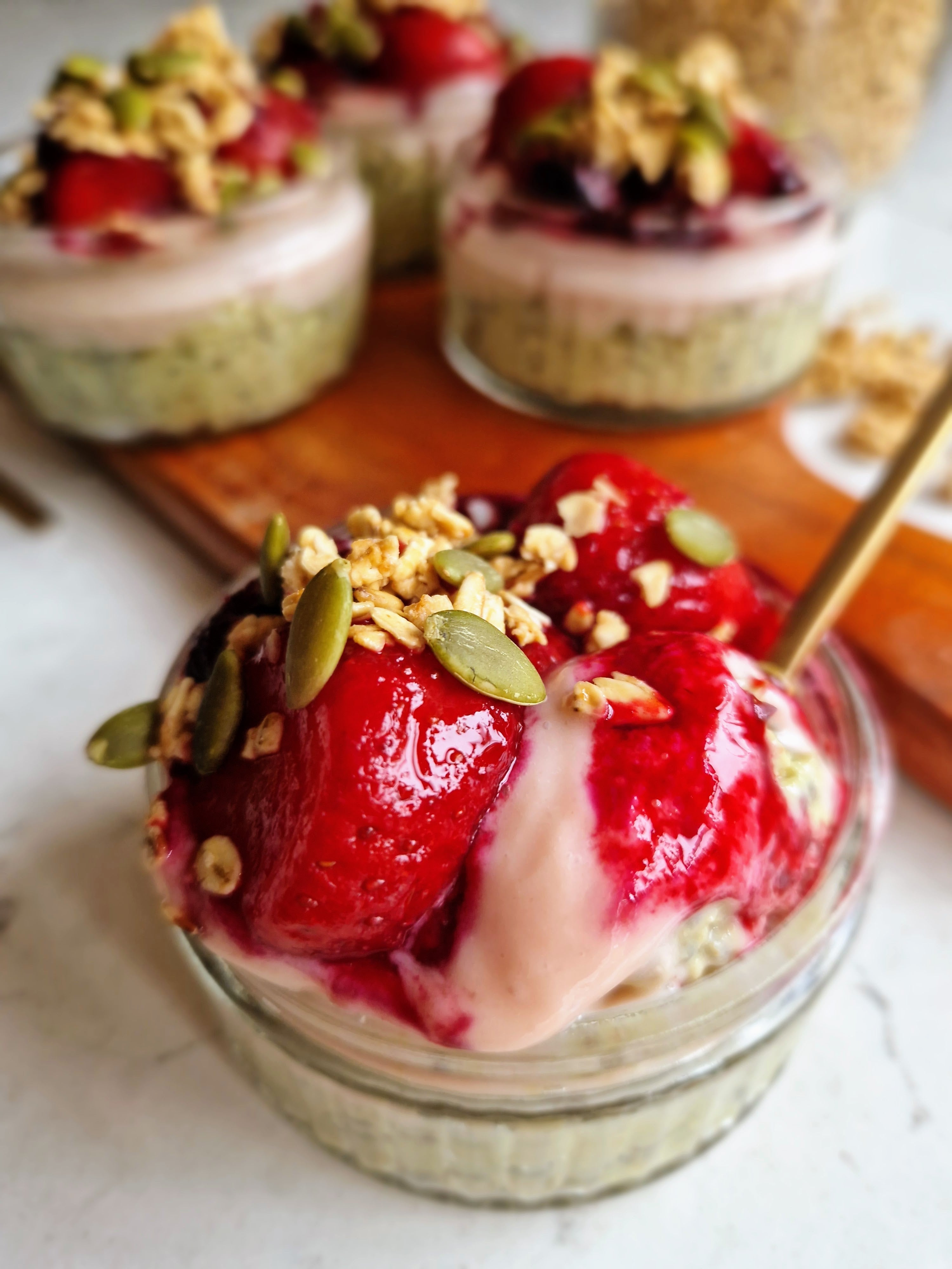3  berry matcha overnight oats in 3 small bowls in the background and a bit unfocused. One bowl of  berry matcha overnight oats at the centre and in front fully focused with a golden spoon.