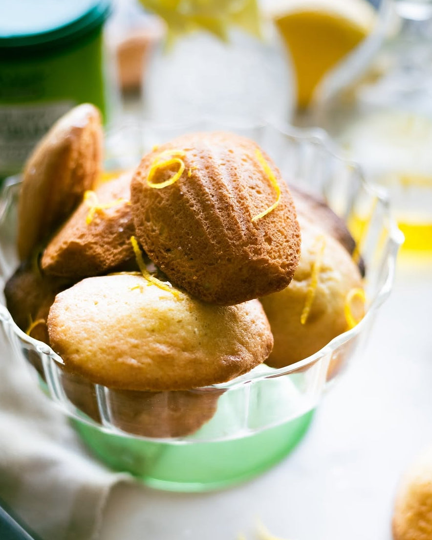 Small lemon muffins in a glass bowl on a light surface with blurred background